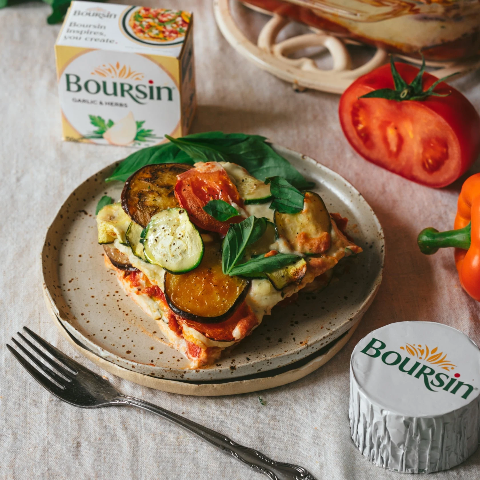 Pizza slice made with vegetables and Boursin cheese, styled on ceramic plate with Boursin cheese and vegetables in background