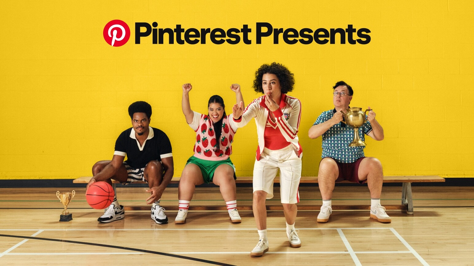 Die Comedians Jeremy Swift, Keyla Monterroso Mejia und Julian Gant posieren auf einer Turnbank vor einer gelben Wand, während Ilana Glazer in eine Pfeife bläst. Darüber ist der Text „Pinterest Presents“ zu lesen. 