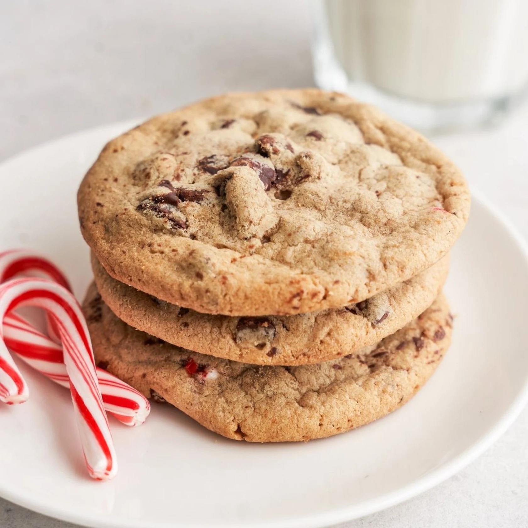 A stack of three chocolate chip cookies sit on a plate next to two candy canes