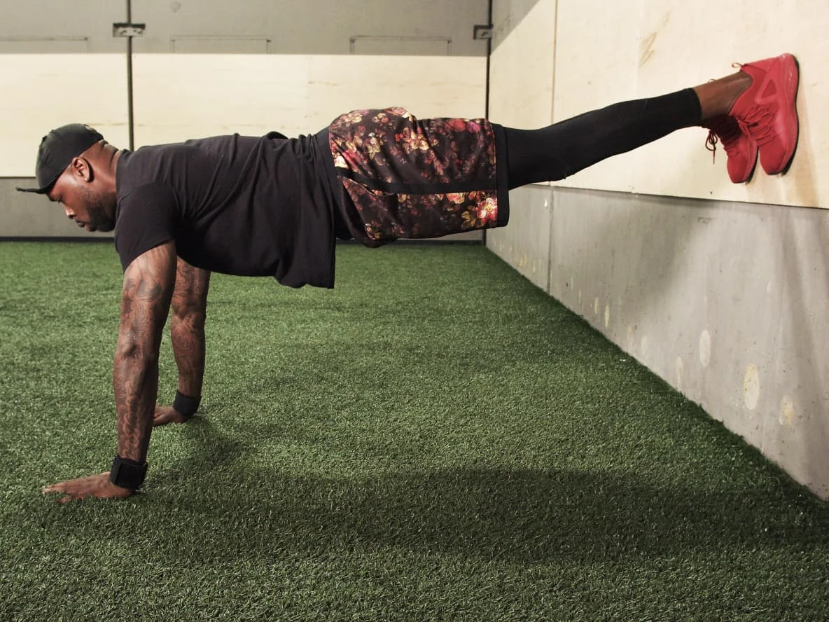 Dennis Dixon does pushups against an indoor wall on artificial grass