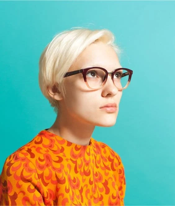 Een witte vrouw met lichtblond haar in een oranje topje die een bril met trendy montuur draagt