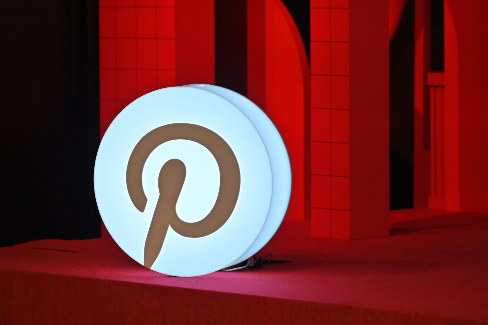 Large illuminated Pinterest “P” logo sign on a red stage, with red geometric set pieces in the background.