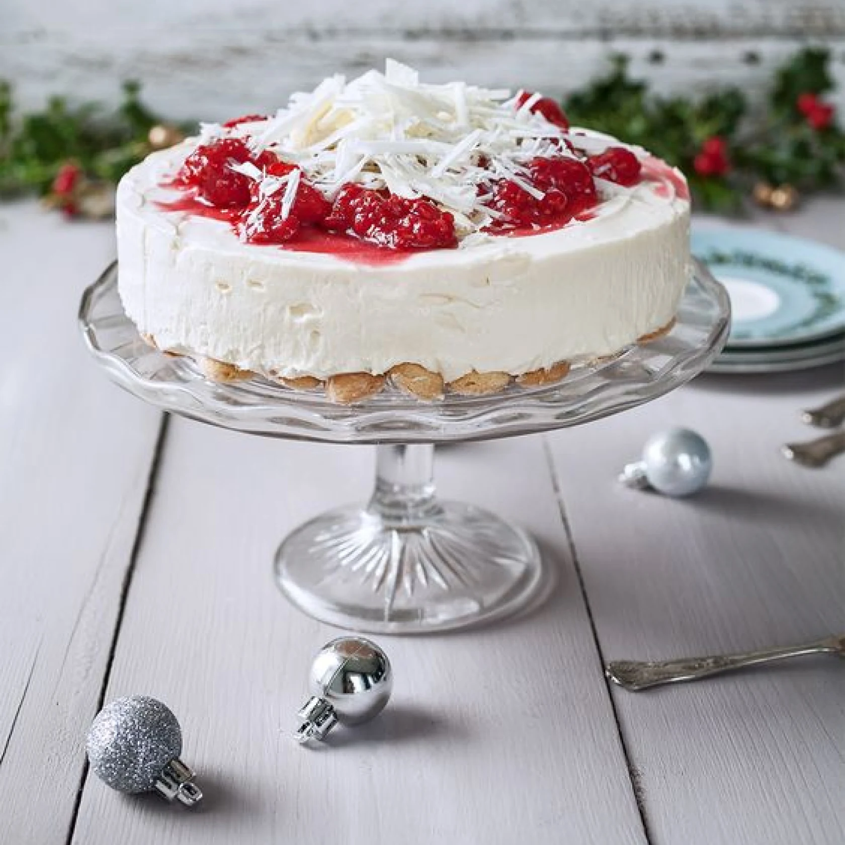 A cheescake covered in strawberries and shave coconut sits on a glass cake stand 