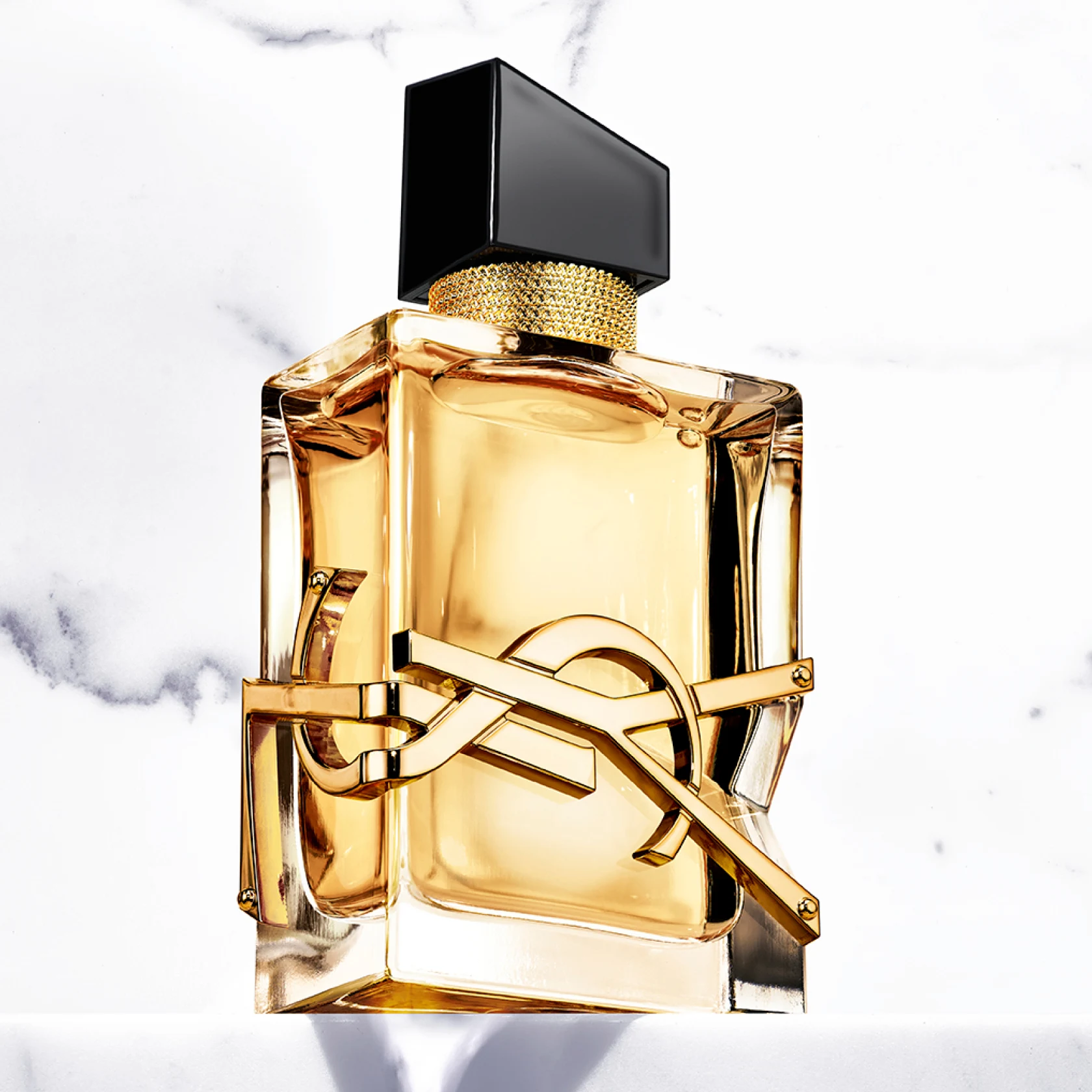 A bottle of perfume sits in front of a marble background 