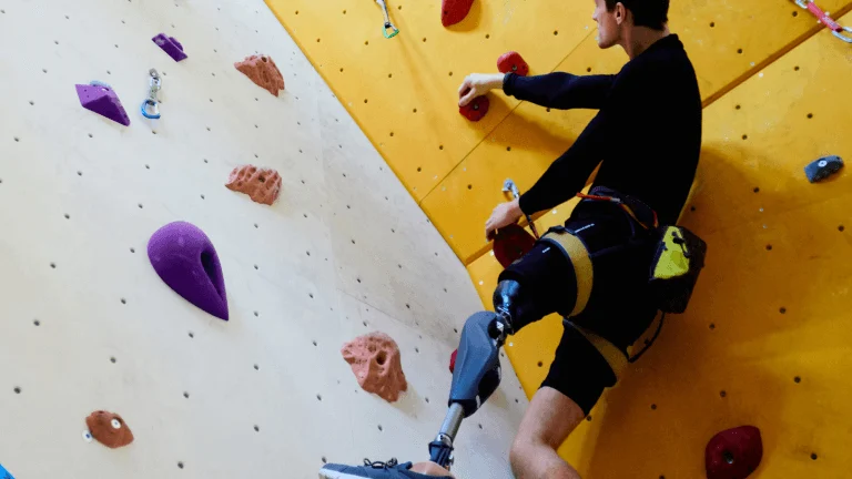 Man with prosthetic leg, dressed in black, ascends a colorful climbing wall