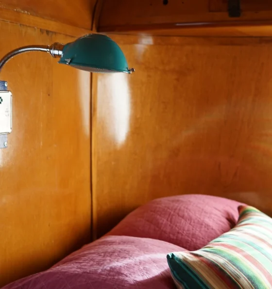 A small camper room with finished wood walls, green wall lamp, and multicolored pillows