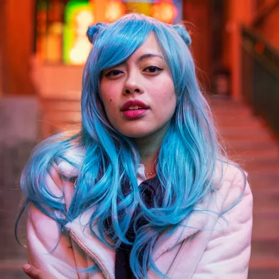 An Asian woman with long blue hair and bright red lipstick wearing a pink coat
