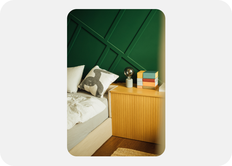 An Image ad features a bed and a wooden nightstand against a green wall. 