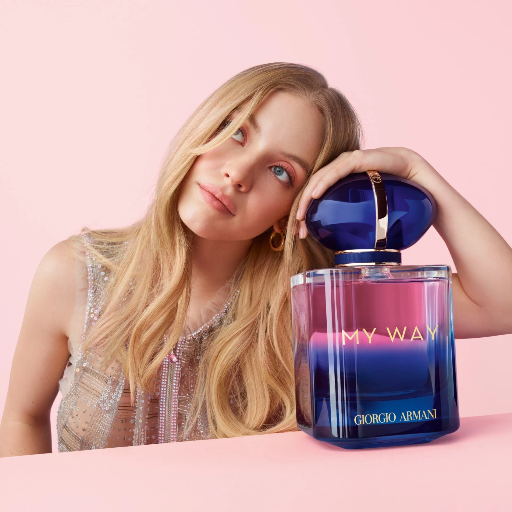 Blonde woman in light pink room leaning on giant bottle of My Way Armani perfume