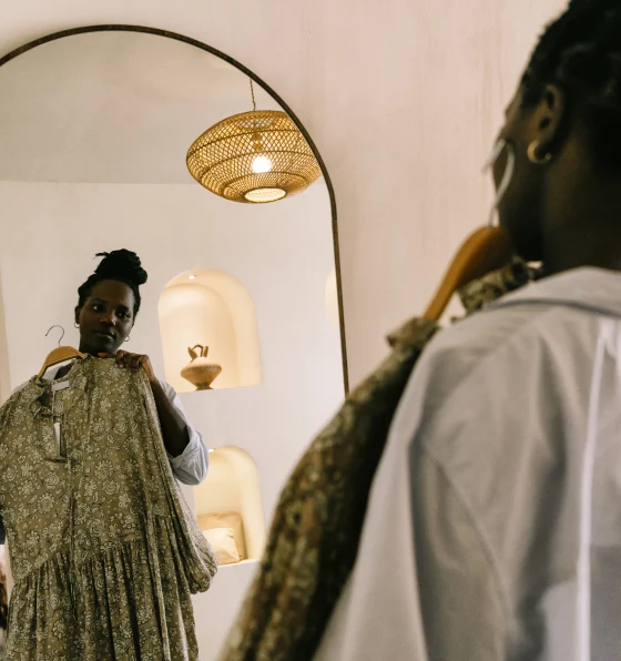 Mulher negra segurando um vestido verde na frente do espelho