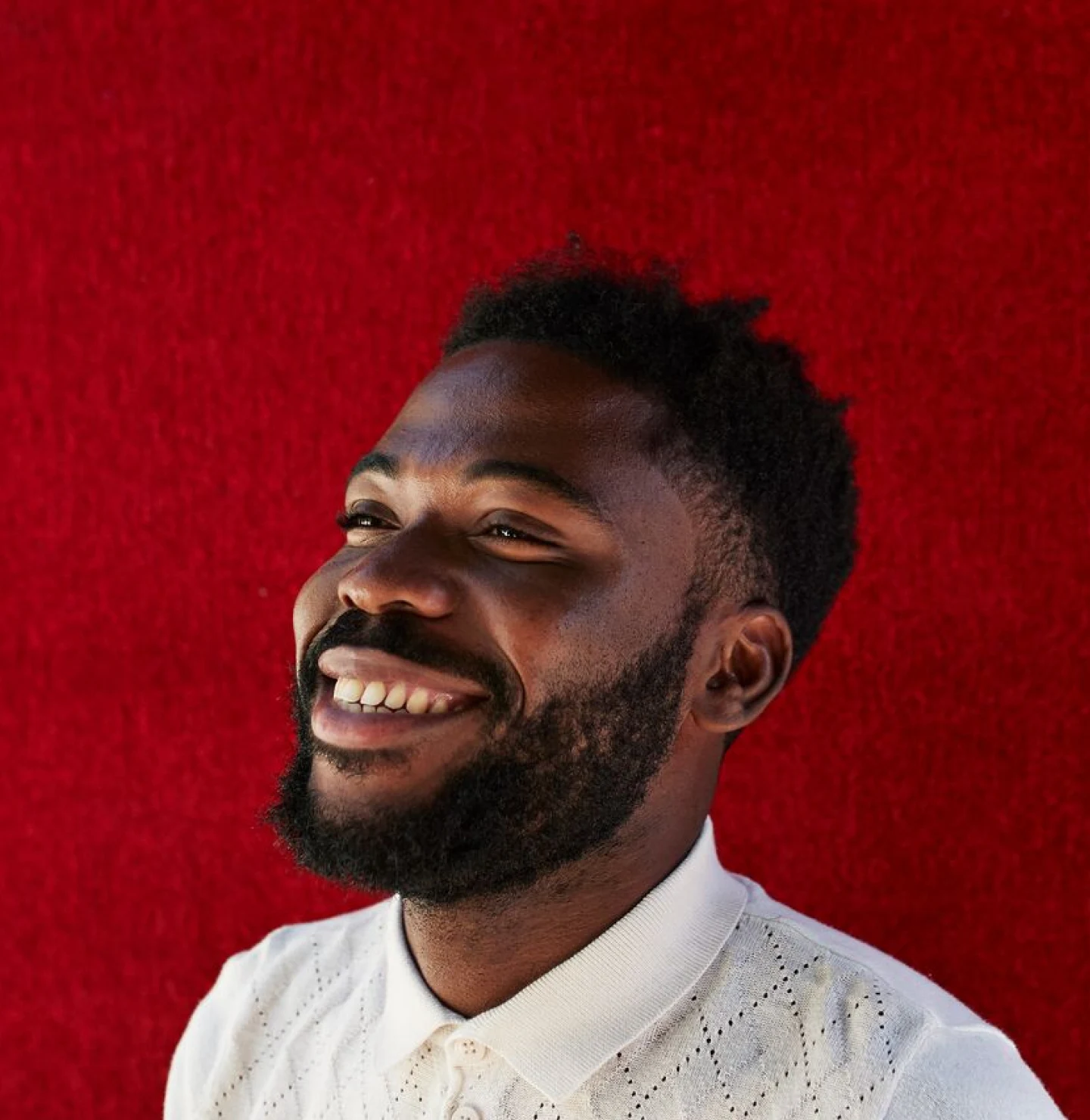 Smiling Black man with a white polo shirt smiles against a red background