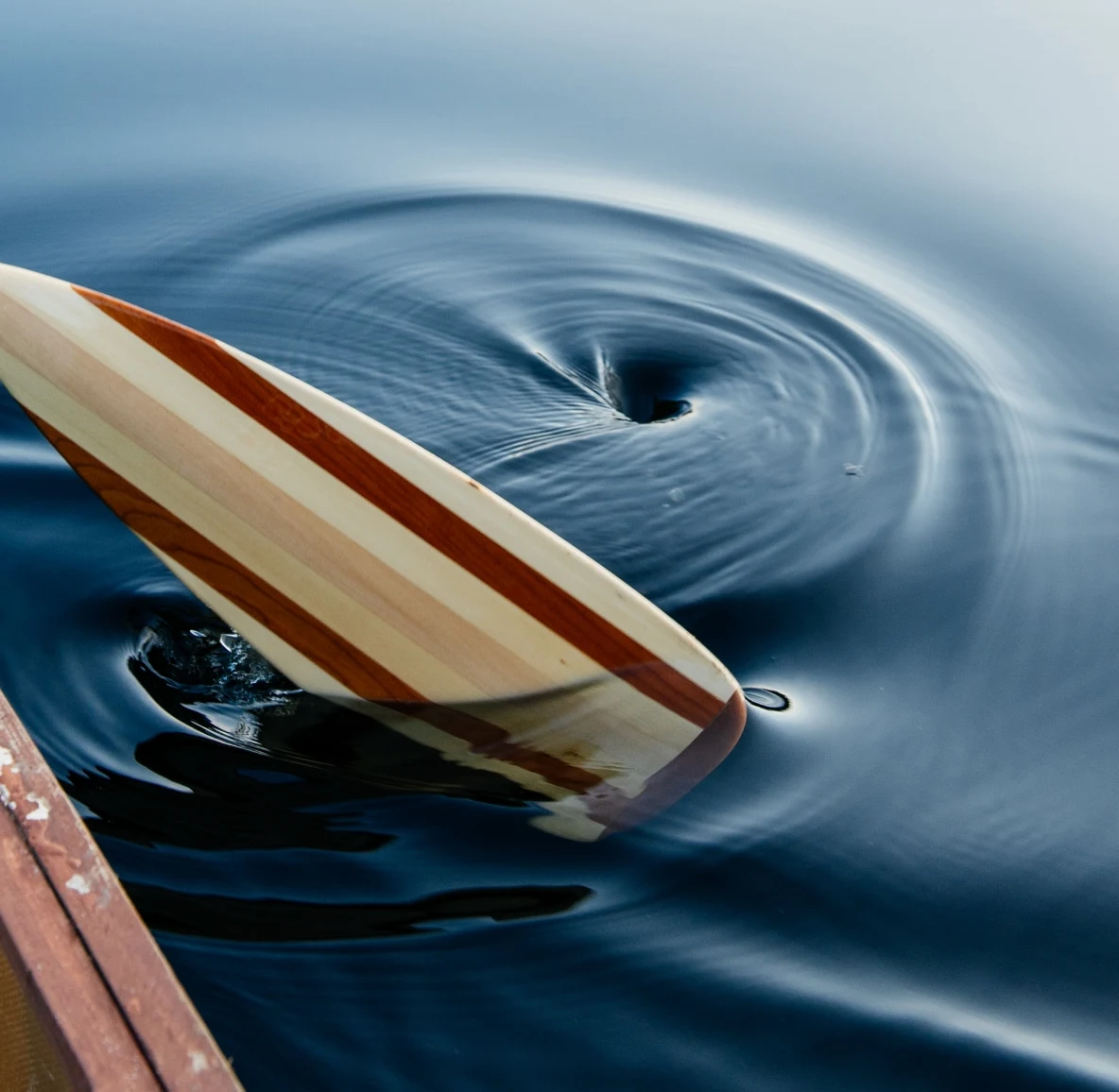 A brown and tan surfboard floats out of a whirlpool of deep blue water