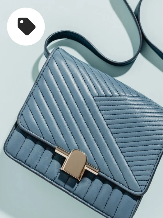 Een lichtblauwe, leren handtas met een lange band in dezelfde stijl. Goudkleurige, metalen details bij de gesp van de tas. 