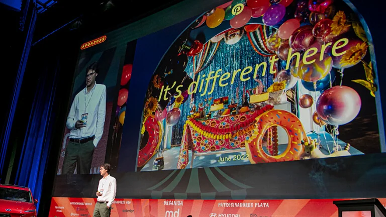 Un empleado de Pinterest da un discurso frente a una pantalla grande que muestra la frase "Aquí es diferente" y el logotipo de Pinterest.