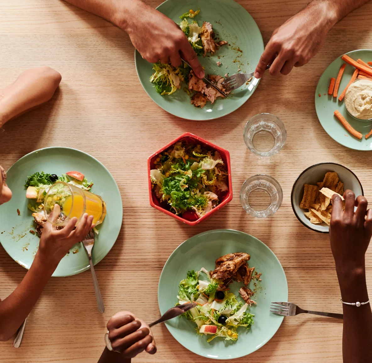 Aerial photo of people’s hands eating salad with chicken on seafoam blue plates