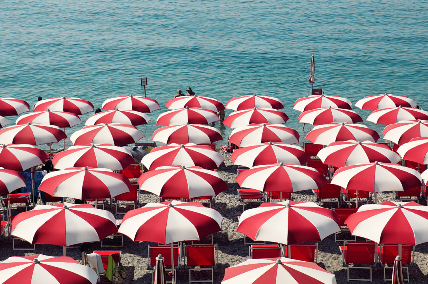 Rows of red and white beach umbrellas and chairs are on a beach