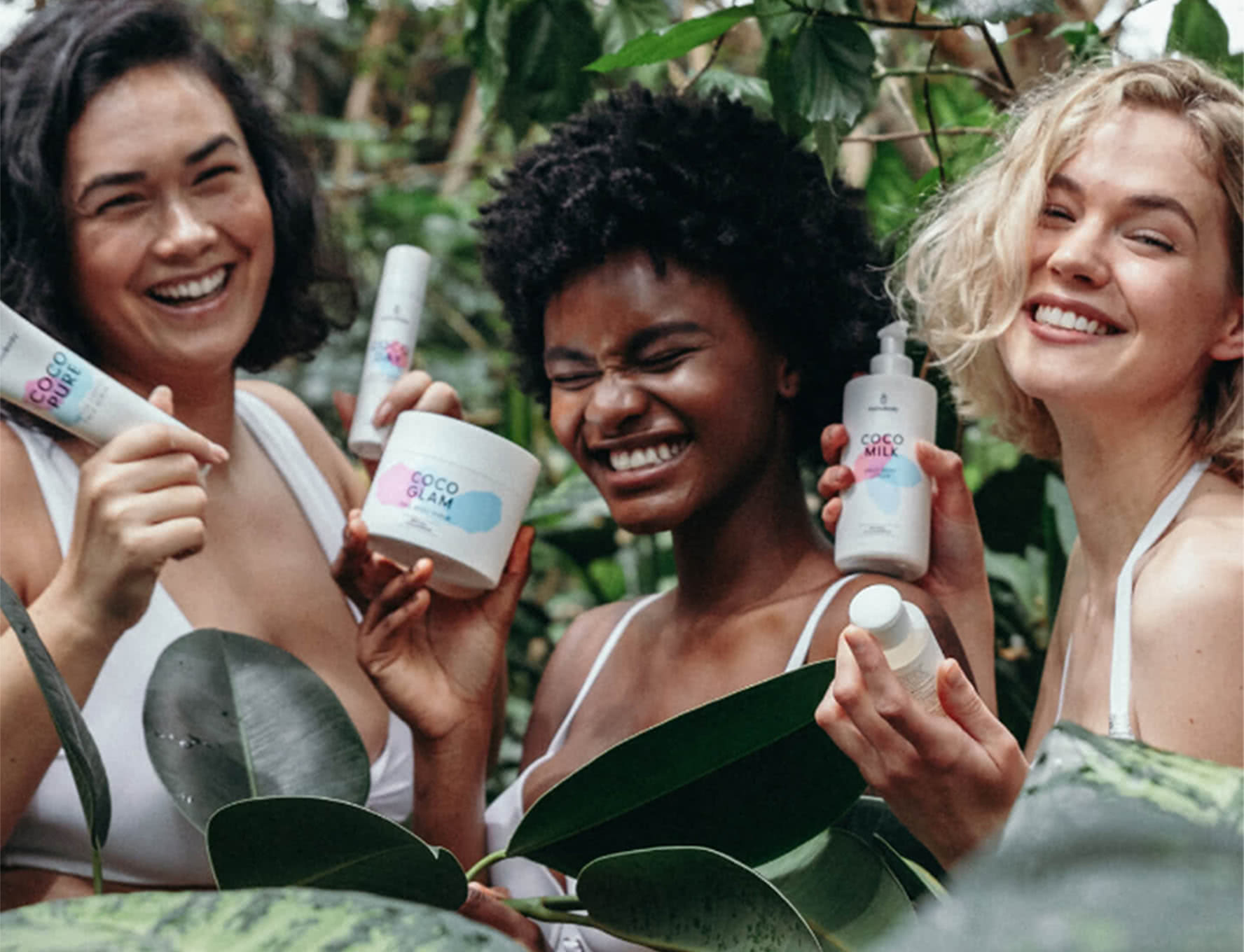 Drei lächelnde Frauen (asiatisch, schwarz und weiß) halten Coco Glam von HelloBody