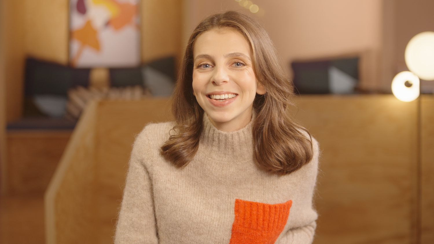 French creator Alix Grousset poses to camera in a light brown sweater featuring a bright orange pocket. 