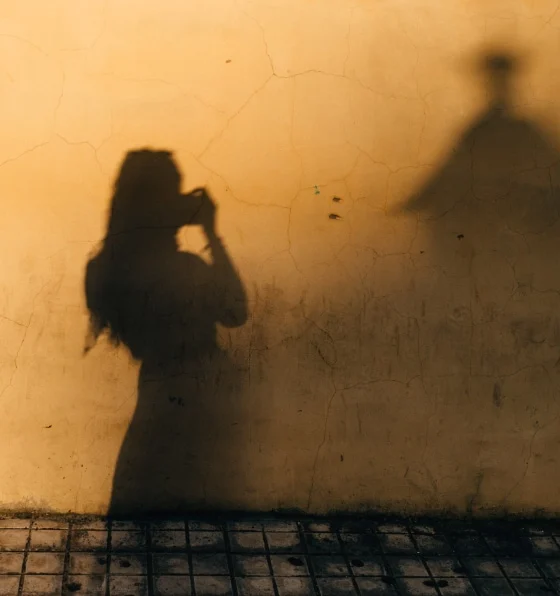 The shadow of a woman taking a picture of herself against a yellow wall