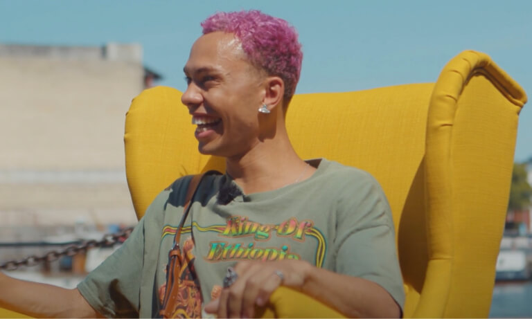 Young Gen Z man with pink hair sits in a yellow chair and laughs 