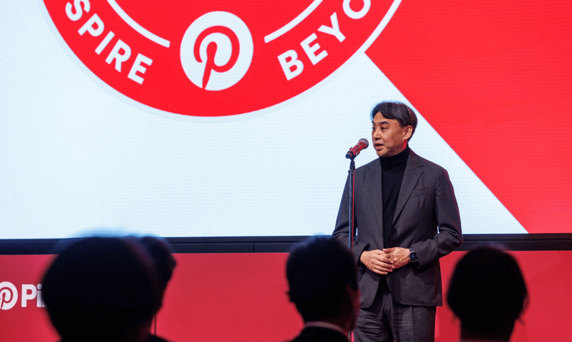 Pinterest Japan Managing Director Takashi Narita in a dark suit stands at a microphone onstage at the PinPro Award 2025, with a large red-and-white Pinterest-themed backdrop and audience silhouettes in the foreground.