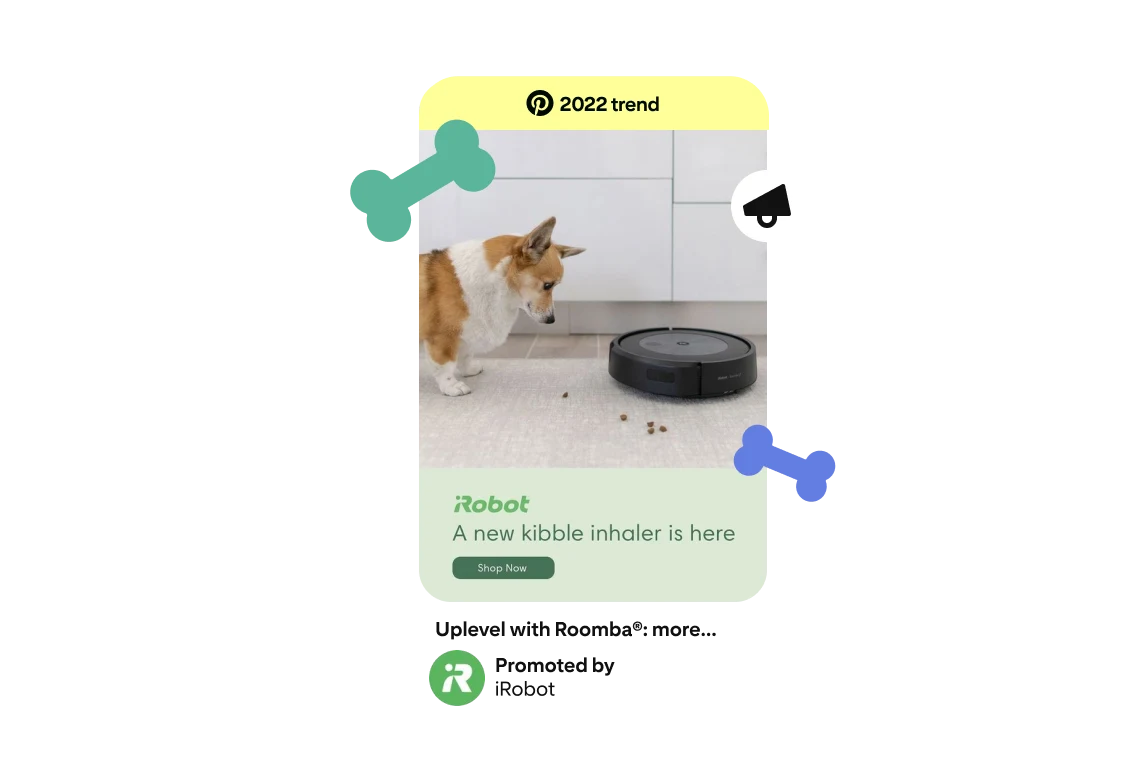 A Pin-shaped ad featuring a Corgi dog with a Roomba vacuum cleaner and kibble sprinkled on the ground. The ad reads ‘a new kibble inhaler is here’ underneath an iRobot logo and a ‘2022 Trend’ badge is featured at the top. 