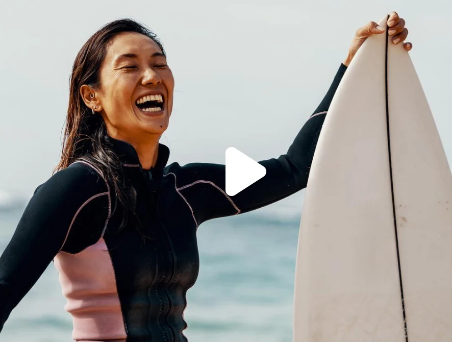 Femme d'Asie de l'Est riant et tenant sa planche de surf à la plage