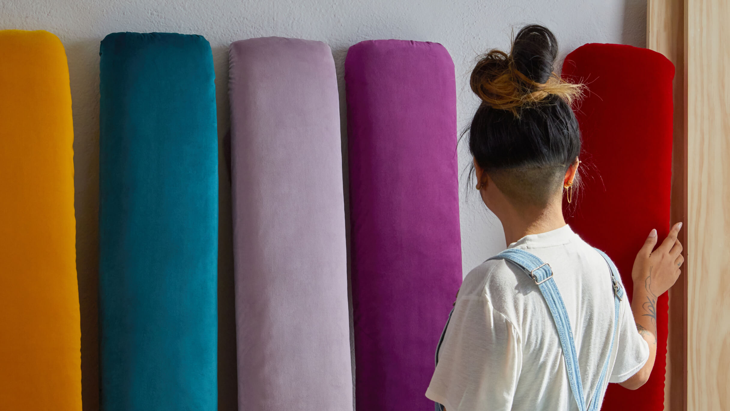 A woman is standing in a shop looking at different coloured bolsters. Her hand is on a red bolster as she considers it.