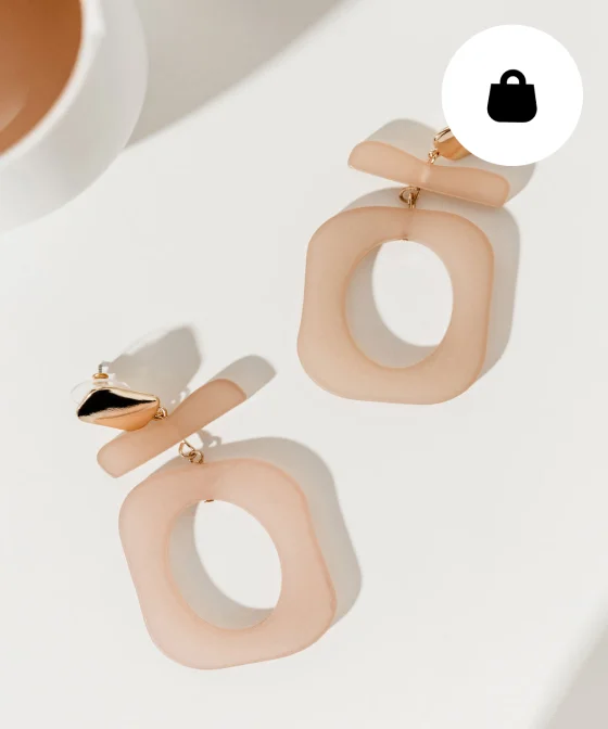 Paire de boucles d’oreilles beige rosé sur fond blanc. 