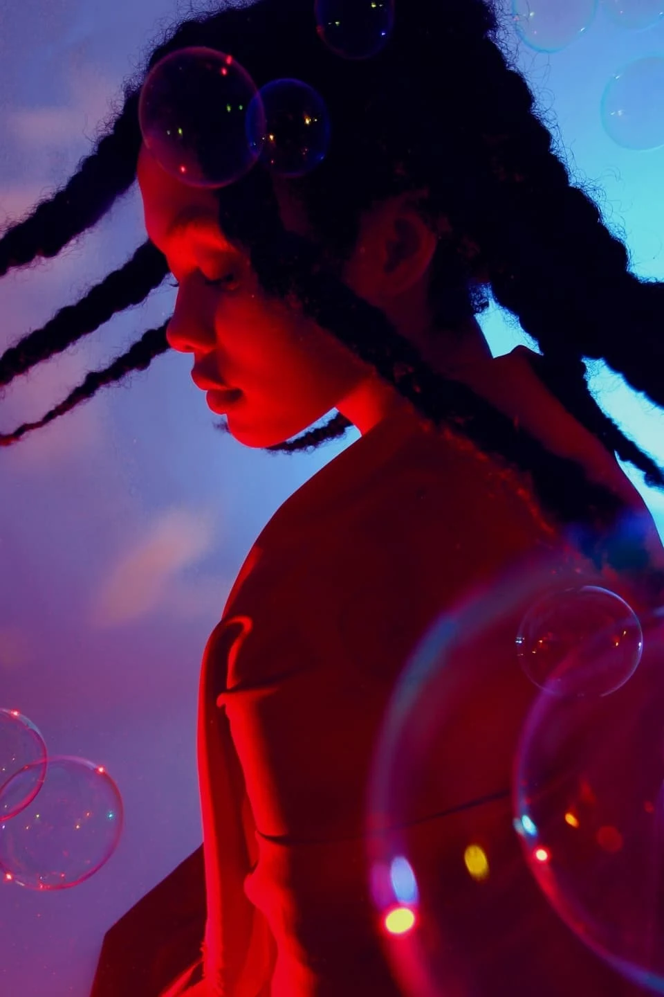 A teenage girl with long braids dancing in blue and purple mood lighting as bubbles float around her