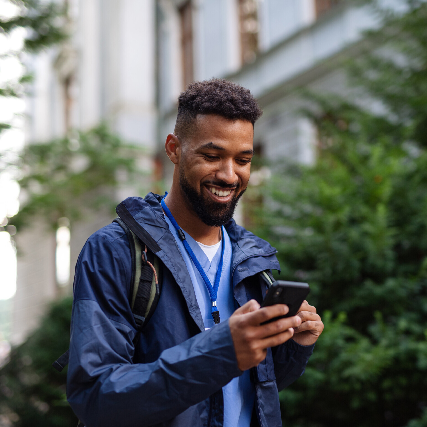 Homem andando lá fora com mochila olhando para o telefone na mão