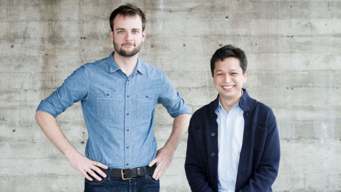 Evan Sharp, medeoprichter en Chief Creative Officer en Ben Silbermann, medeoprichter en CEO staan voor een grijze bakstenen muur