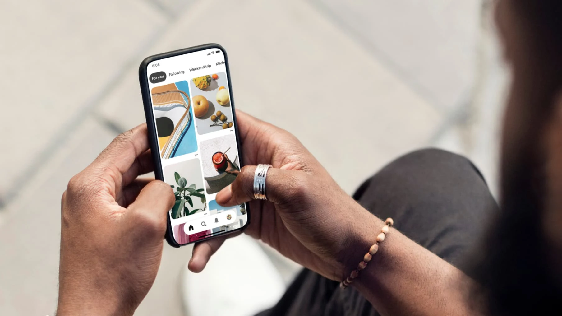 Egy fekete férfi válla fölül készített kép, melyen éppen a pinjeit böngészi a mobilján