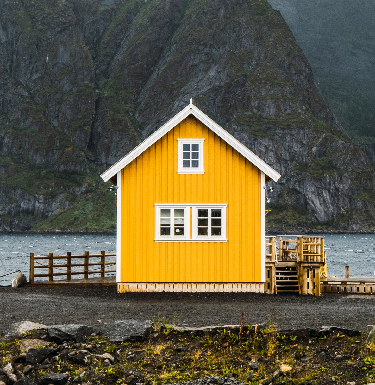 A small yellow A-frame lake house, set against a rocky green mountain in the background