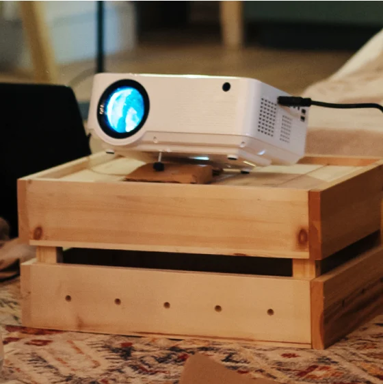 A shot of a projector on top of a wooden box placed in a bedroom.