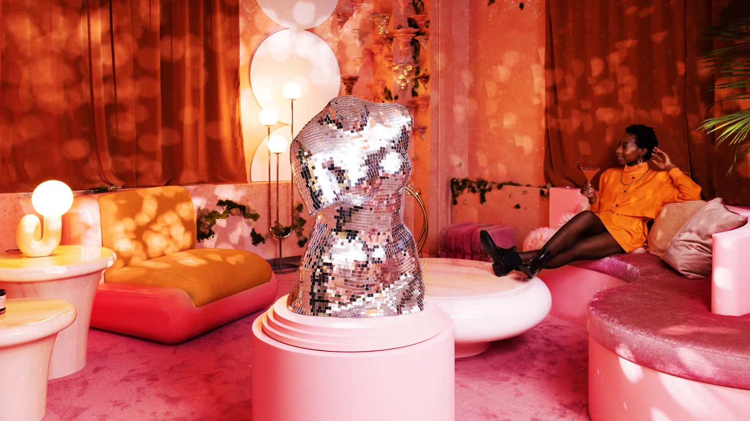 Black woman sitting in a luxuriously pink, orange and blingy conference room.