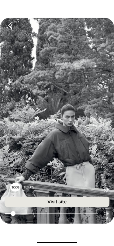 Black-and-white image of a fashionable person in a jacket and skirt, leaning on a banister in a lush garden setting. The mood is stylish and serene.