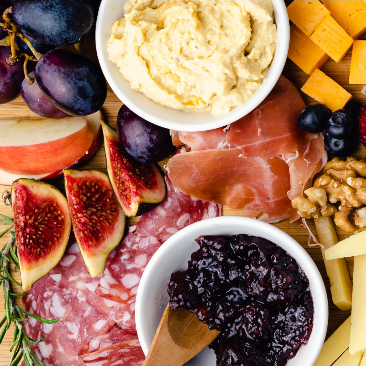 Closeup shot of a grazing board featuring figs, cured meats, jams, hummus, cheese and assorted nuts.