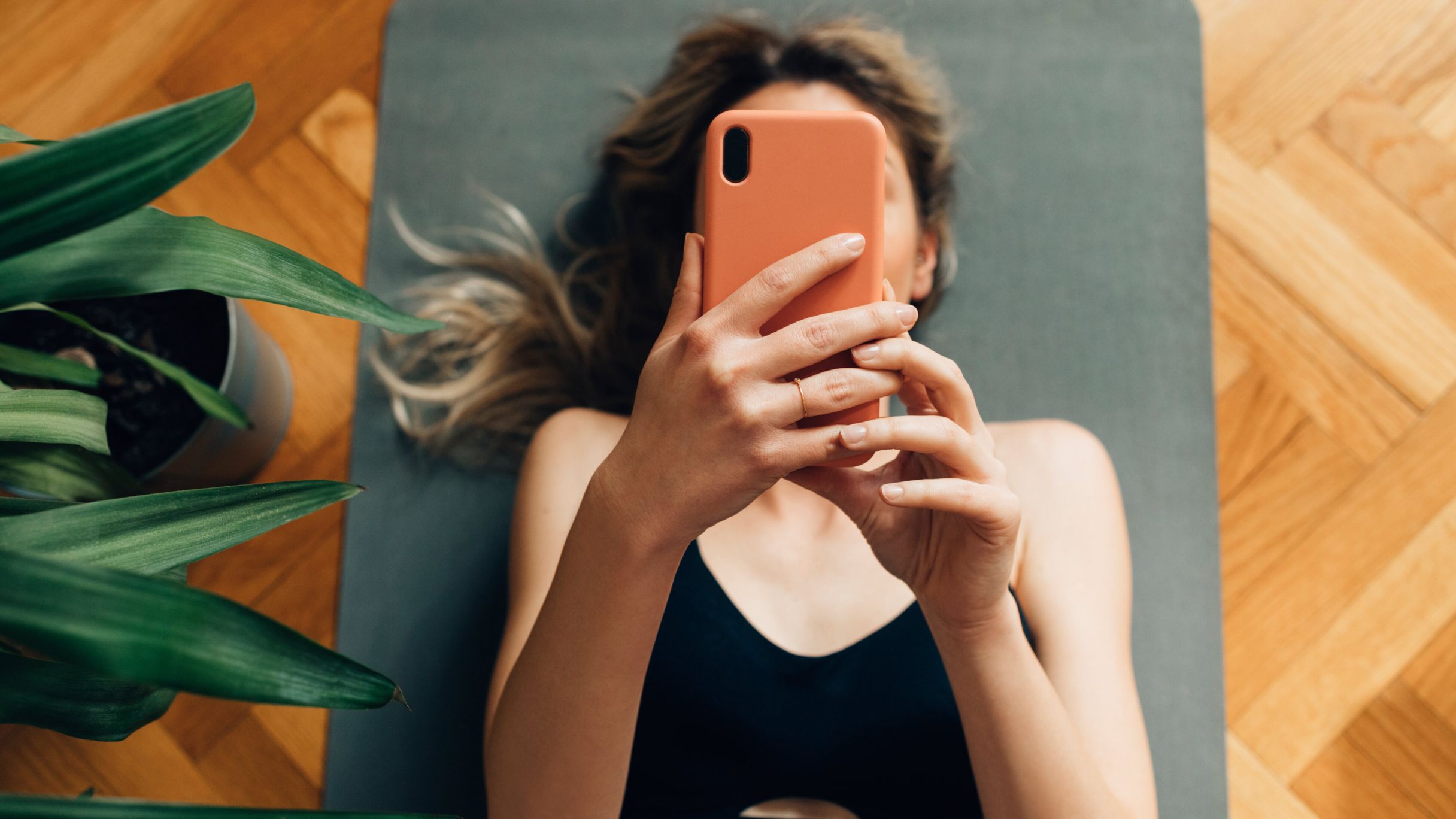 A white woman browsing on a cell phone while lying on a grey yoga mat.