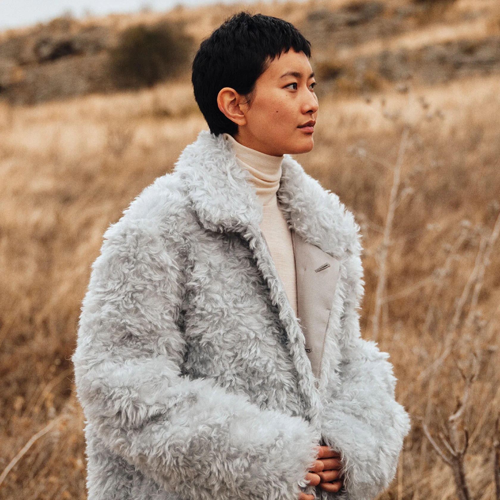Asiatisches Model mit Pixie-Schnitt modelliert im Weizenfeld und trägt eine flauschige graue Jacke und Rollkragenpullover