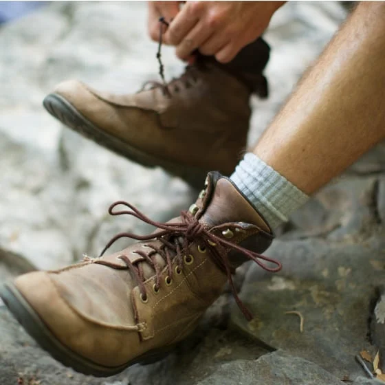 Close-up on brown hiking boots against rocks, the shoelaces being tied by white hands