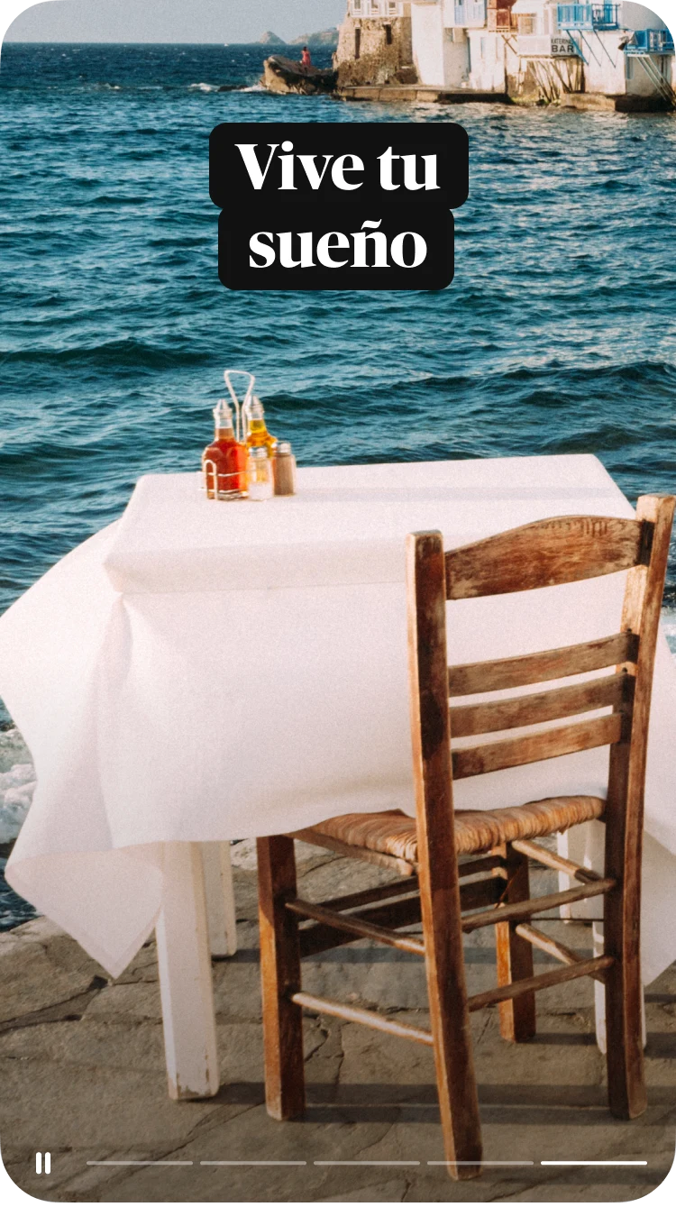 Una mesa dispuesta para uno en un café al aire libre, cubierta con un mantel blanco; en el fondo, se ven el mar y edificios, y el texto superpuesto es "Vive tu sueño"