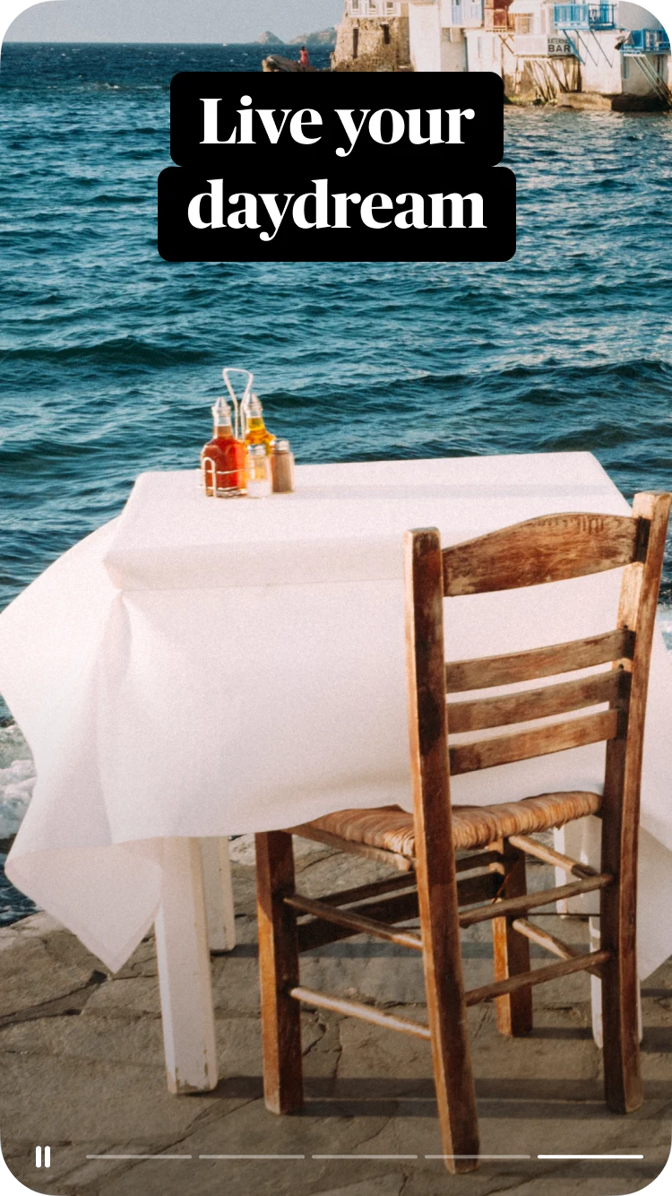 Uma mesa de café ao ar livre coberta por uma toalha branca, o mar e edifícios como pano de fundo, com um texto sobreposto que diz "Vive o teu sonho"