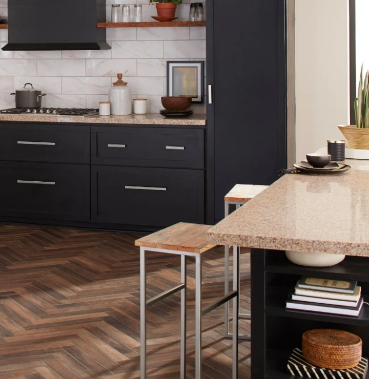 A modern kitchen with dark wood cabinets, white tiled walls, parquet flooring and a beige quartz countertop