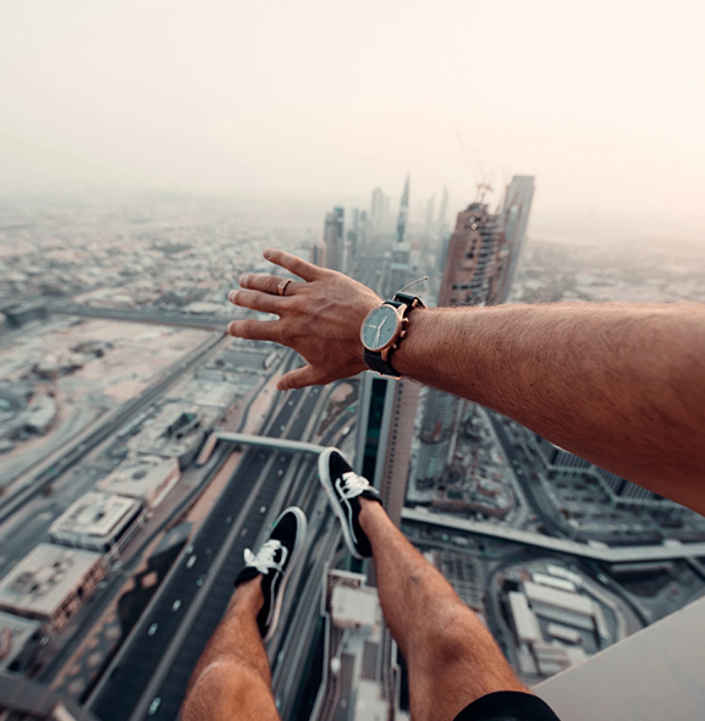 Dangling legs in black sneakers and a wrist-watched arm above a vast cityscape