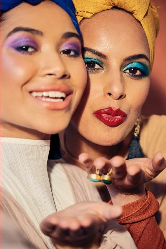 Two women wearing bright eyeshadow and lipstick