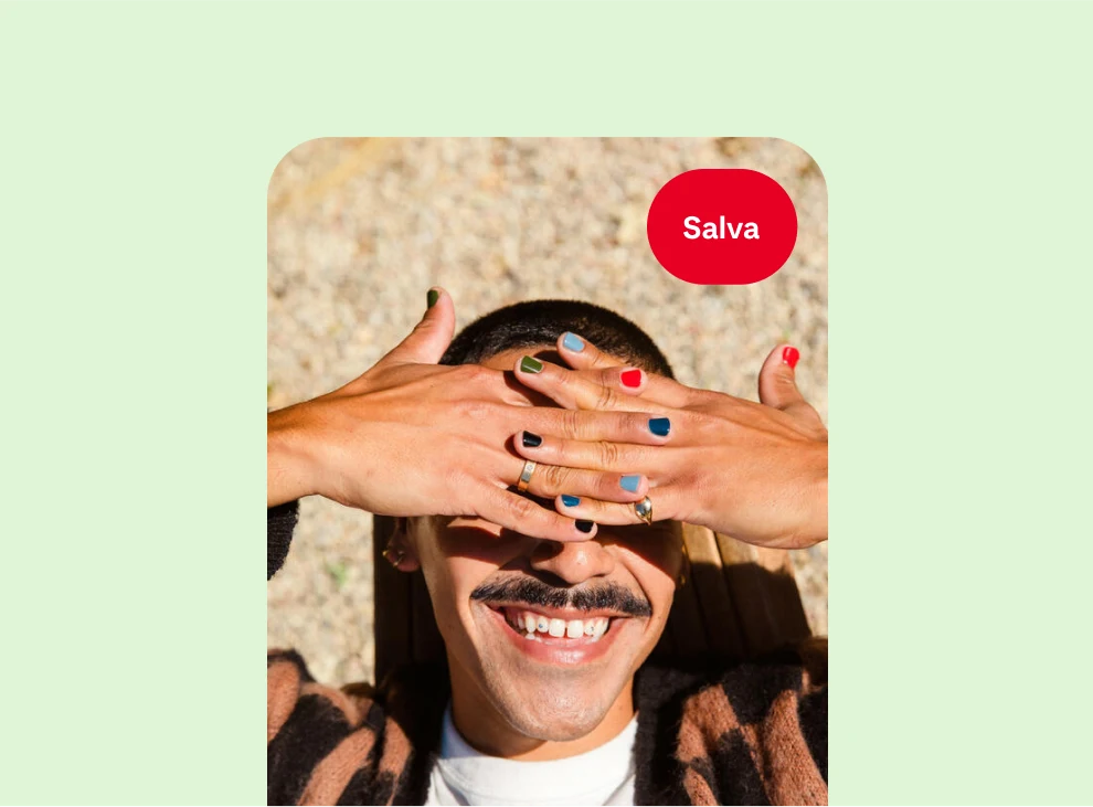 Una persona bianca sorridente che protegge i propri occhi dal sole: le unghie delle mani sono dipinte ognuna di un colore diverso di smalto.