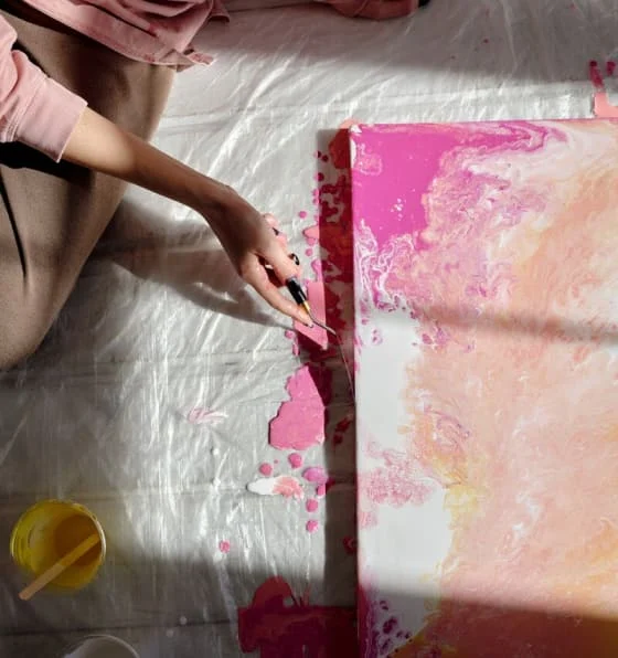 A painter touches up the edge of a canvas showing various shades of pink on white