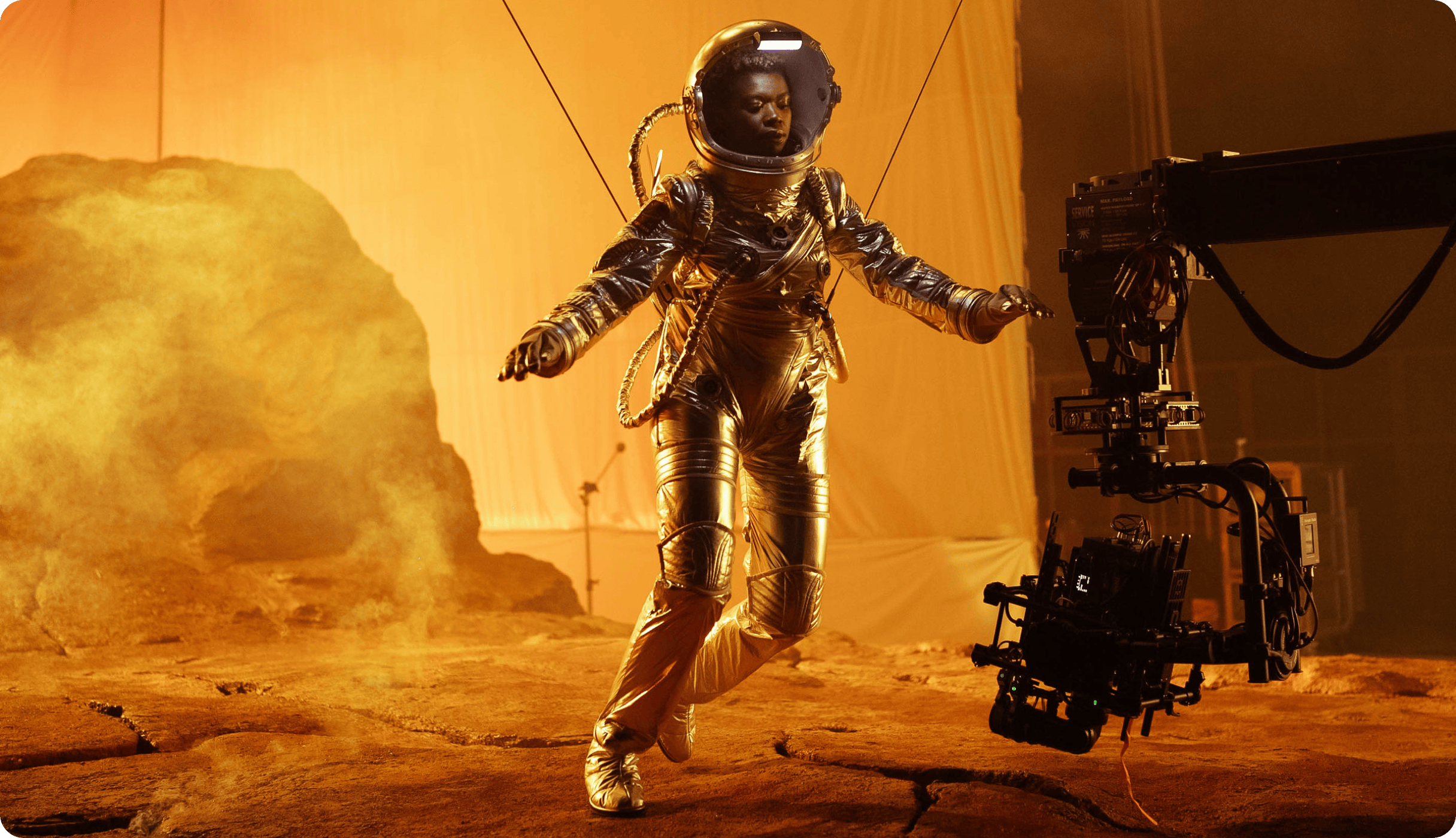 A woman in an astronaut suit poses on a set, posed in front of space rocks.