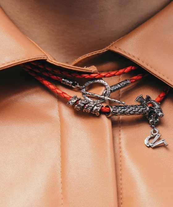 Image of a red necklace with metal detailing on a neck, worn over a tan, pleather collared shirt. 